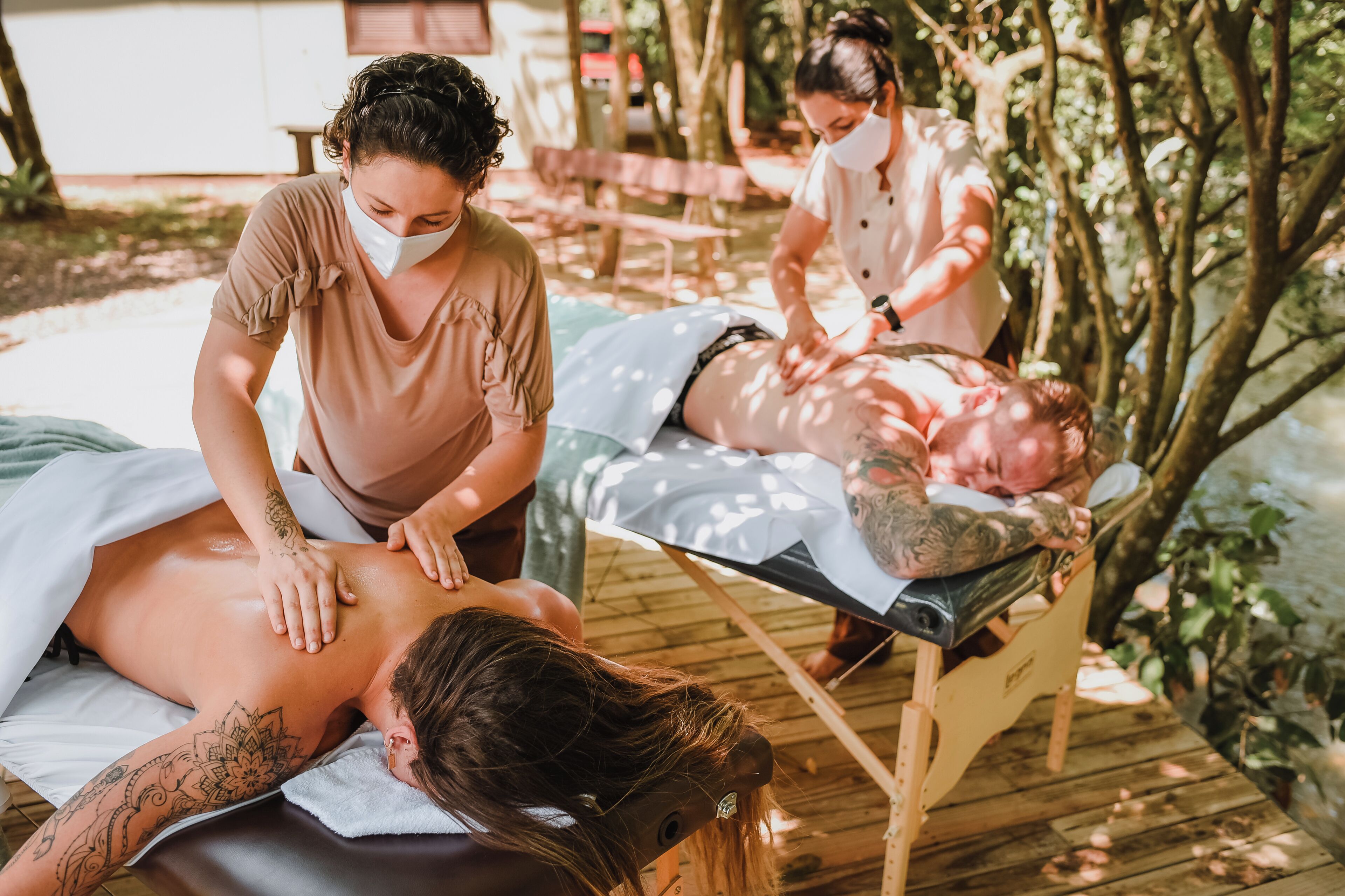 A massage therapy session in an outdoor setting with wooden deck flooring and greenery in the background.