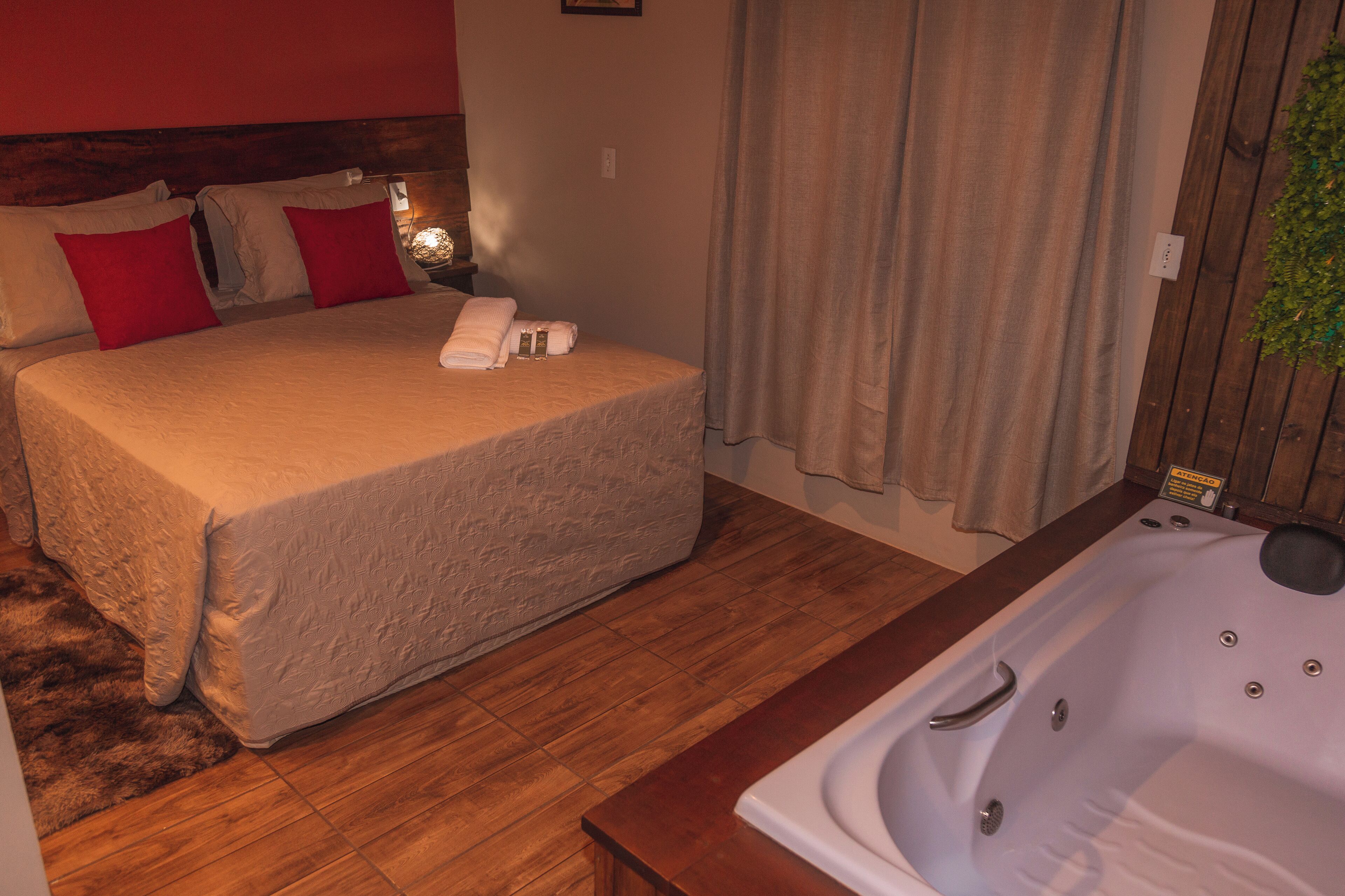 Ein Schlafzimmer mit einem großen Bett, einem Holzkopfende, Holzboden, einem Badezimmer mit Badewanne und einer Topfpflanze.