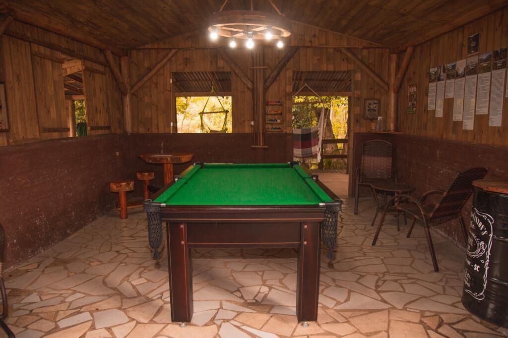 A pool table in a wooden room with stone flooring, wooden walls, and a hanging light fixture.