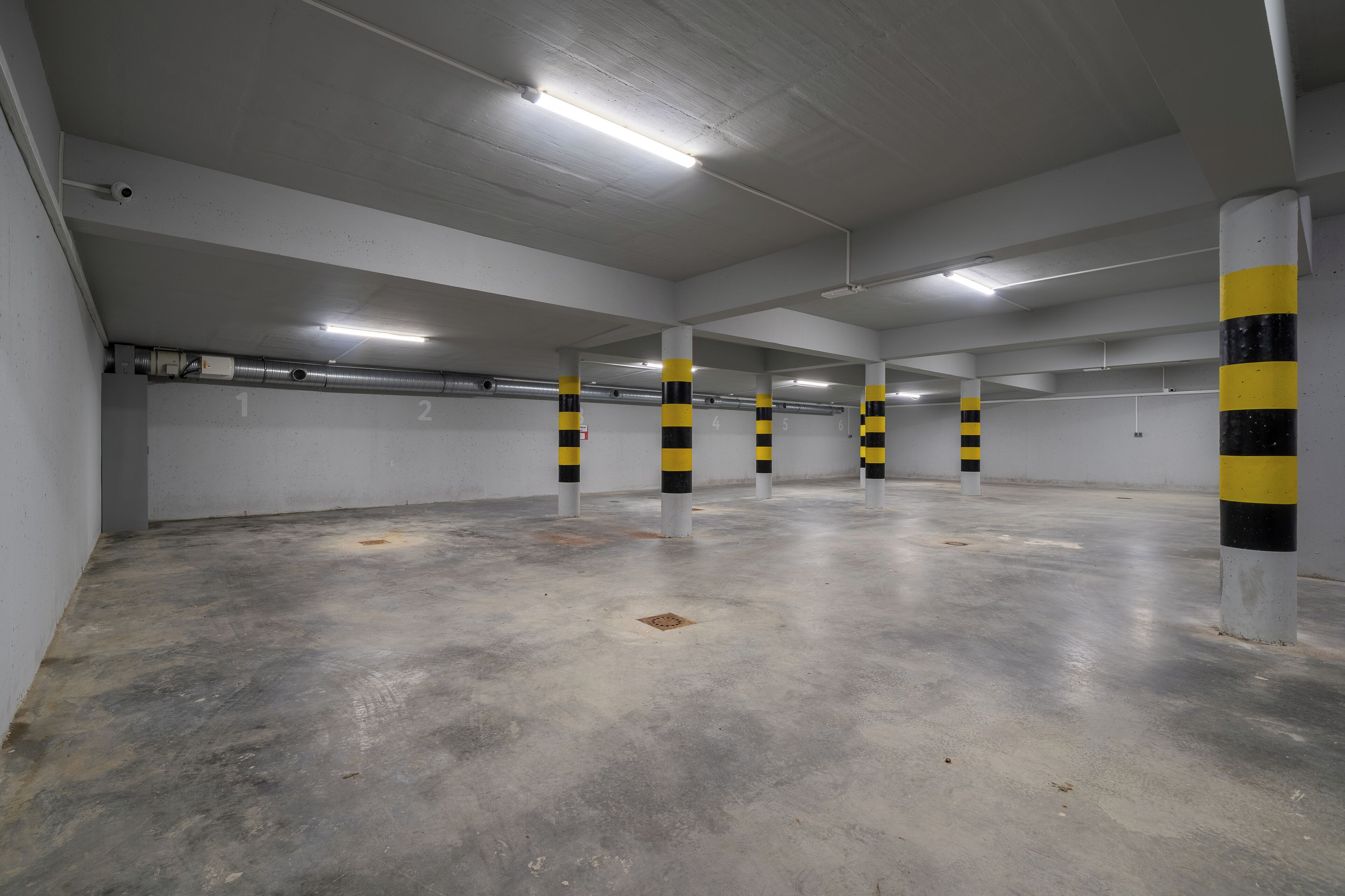 Um estacionamento multi-andar com pisos de concreto e paredes brancas, com pilares listrados em amarelo e preto.