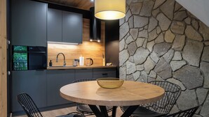 Una cucina moderna con mobili scuri, una parete in pietra e un tavolo rotondo in legno con sedie.
