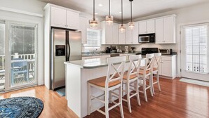 A modern kitchen with white cabinets, stainless steel appliances, and bar stools. - Spacious 4 Bedroom, Sleeps 10. Walk everywhere! (Bethany Beach)