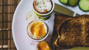 A plate with two halves of an egg, a slice of toast, and a knife. - Hotel Vashistha (Prayagraj)