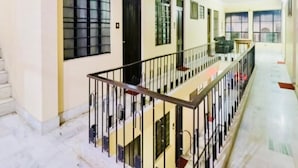 A spacious corridor with a central staircase, multiple windows, and a balcony on the upper level. - Hotel Vashistha (Prayagraj)