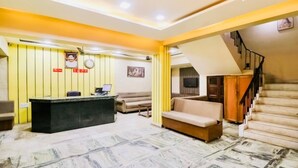 A hotel lobby with a reception desk, sofas, a staircase, and a tiled floor. - Hotel Vashistha (Prayagraj)