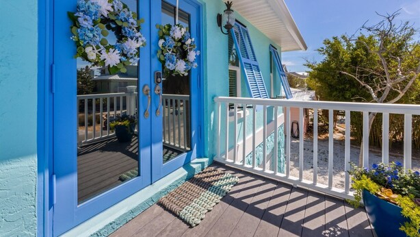 Een huis met een turquoise gevel, een witte veranda, blauwe luiken en een witte balustrade.