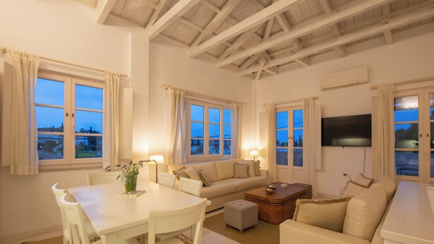 A well-lit living room with a dining table, white chairs, a sofa, and a television.