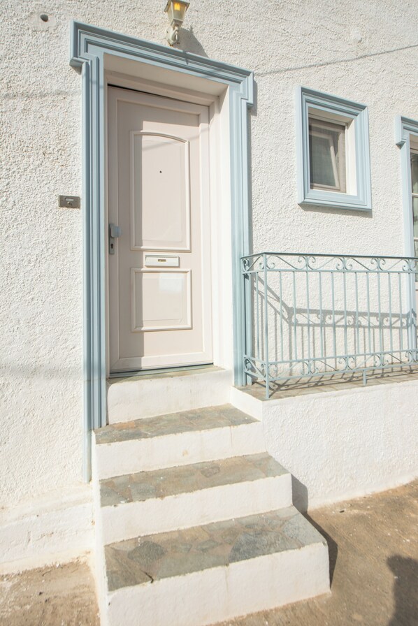 A white building with a white door and a small window. There are steps leading up to the door.