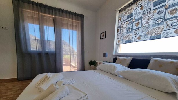 Hotellihuone, jossa on suuri sänky, ikkunasta avautuva kaunis näkymä ja yöpöytä, jossa on lamppu.