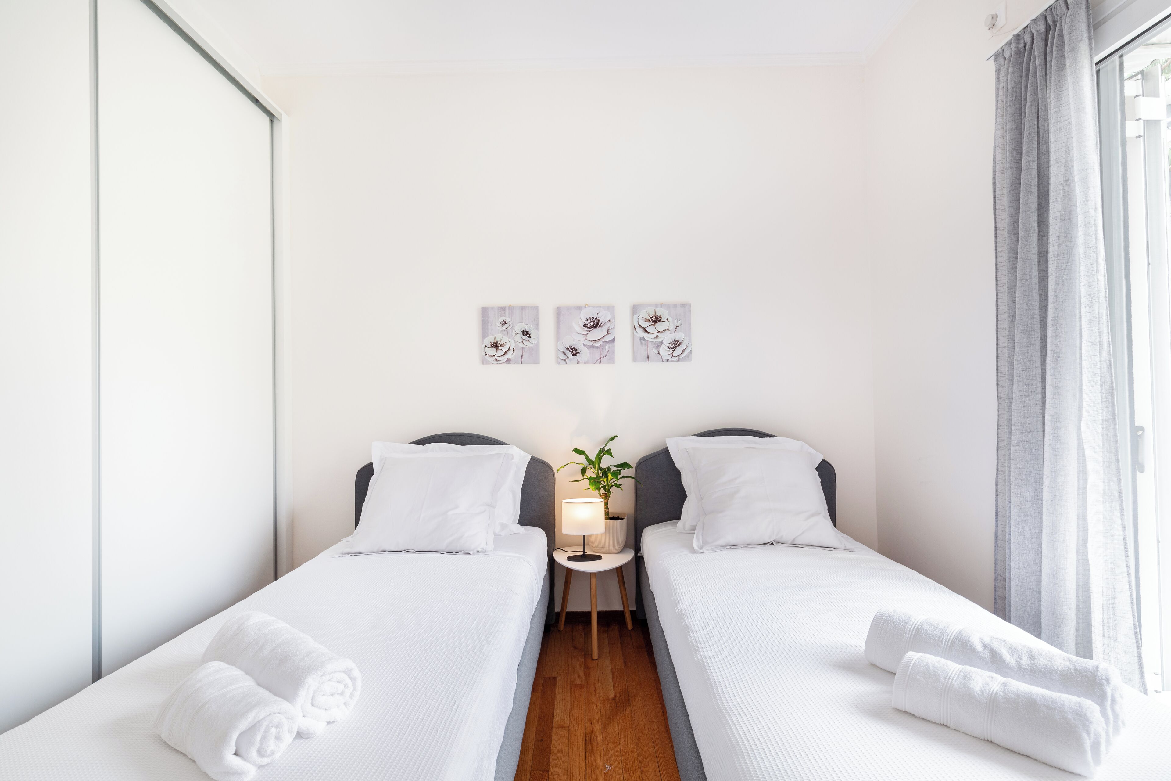 A hotel room with two beds, a small table with a lamp, and three wall-mounted pictures.