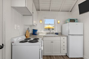 A compact kitchen with white cabinetry, a stove, a sink, and a refrigerator. - Waterfront Cottage With Lovely Patio (2382) (Truro)