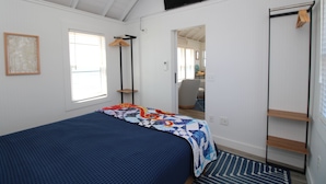 Ein Schlafzimmer mit Bett, Fenster, Tür und einem Fernseher an der Wand.