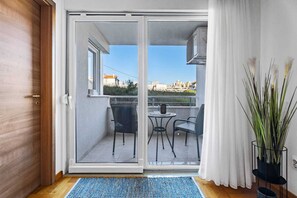 A sliding glass door leading to a balcony with a table and chairs, a potted plant, and a view of buildings in the distance. - Apartment Maya by Litto (Split)