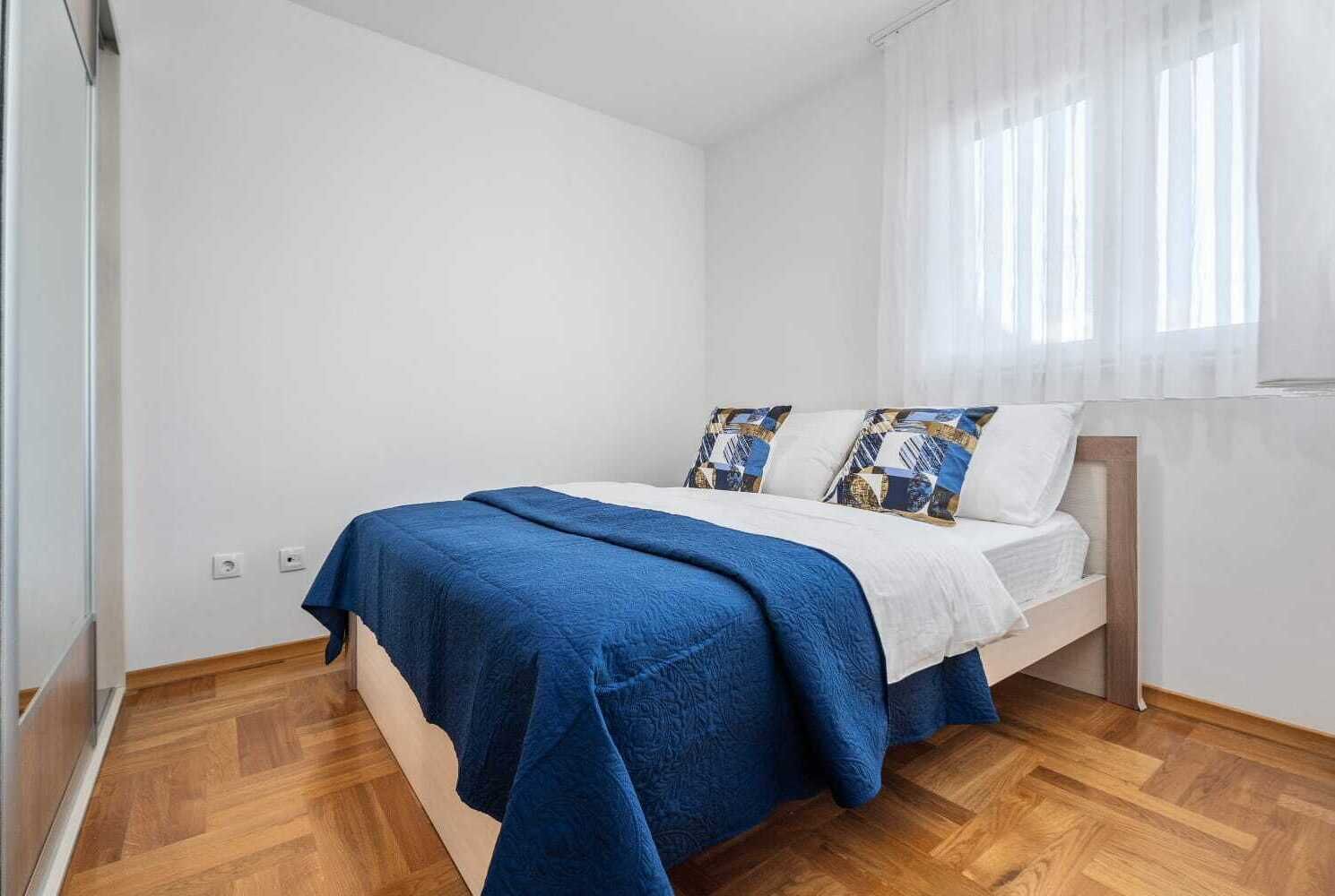 Egy hálószoba, amelyben egy ágy, egy kék takaró és mintás párnák találhatók.
