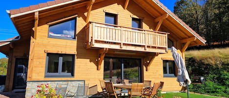 A wooden cabin with a balcony, outdoor seating, and a garden area.