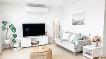A modern living room with a flat-screen TV, a grey sofa, a round coffee table, and a white side table.