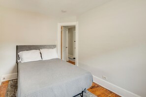 Una camera da letto con un letto, pavimento in legno e una porta bianca che dà su un'altra stanza.