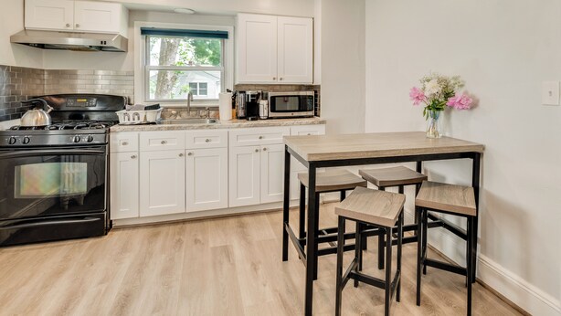 Une cuisine avec des meubles blancs, une cuisinière noire, un four à micro-ondes et une table en bois avec des tabourets de bar.