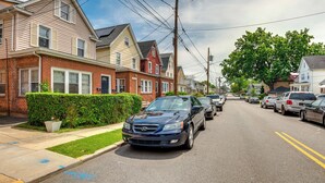 Une rue résidentielle bordée de maisons, de voitures garées et d’une haie.