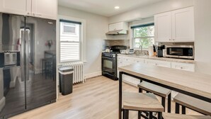Une cuisine moderne avec des meubles blancs, un réfrigérateur en acier inoxydable, un four encastré, un four à micro-ondes et une table à manger en bois avec des bancs.