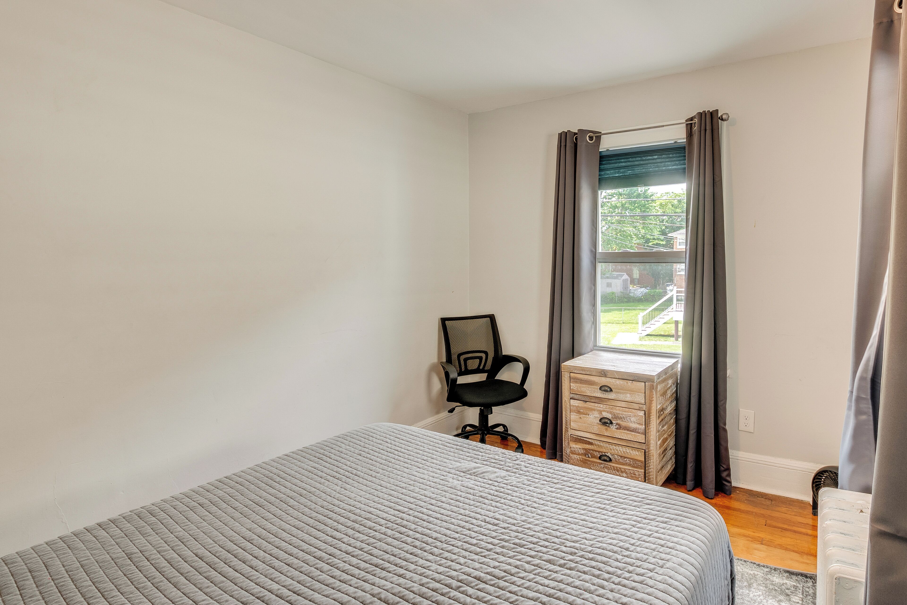 A bedroom with a bed, a desk, a chair, and a window with curtains.
