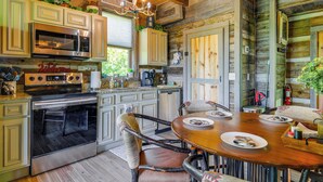 A rustic kitchen with wooden cabinets, a stainless steel oven, and a wooden dining table with chairs. - Hot Tub + Pool Table: 3-story Gatlinburg Cabin! (Gatlinburg)