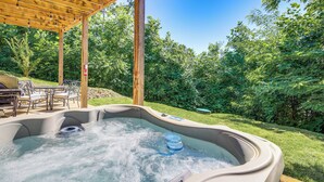 A hot tub under a wooden pergola with a patio area and outdoor furniture. - Hot Tub + Pool Table: 3-story Gatlinburg Cabin! (Gatlinburg)