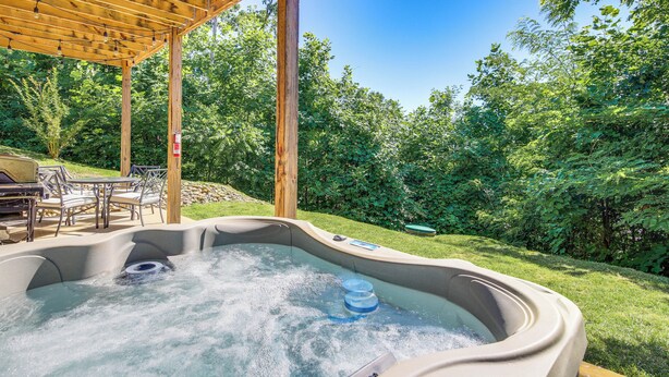 A hot tub under a wooden pergola with a patio area and outdoor furniture. - Hot Tub + Pool Table: 3-story Gatlinburg Cabin! (Gatlinburg)