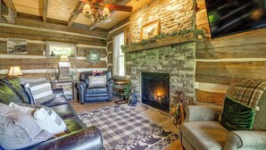 A cozy log cabin interior with a fireplace, leather sofas, and a stone wall. - Hot Tub + Pool Table: 3-story Gatlinburg Cabin! (Gatlinburg)
