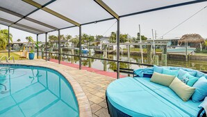 Un espace piscine abrité, avec un fauteuil de relaxation et une petite table, une vue dégagée sur une étendue d’eau, et un bâtiment à toit de chaume en arrière-plan.