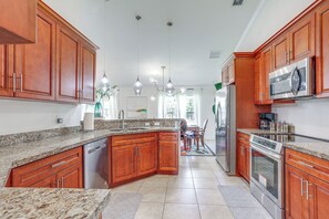 A modern kitchen with granite countertops, wooden cabinets, stainless steel appliances, and pendant lighting.
