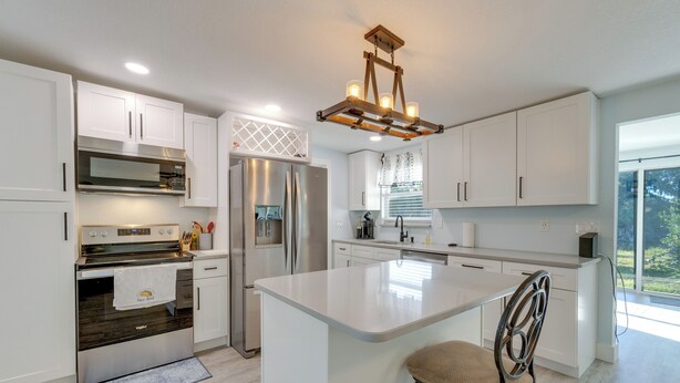 A modern kitchen with white cabinetry, stainless steel appliances, and a central island with a chair.