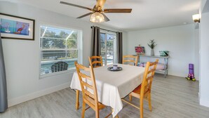 A dining area with a table, chairs, a ceiling fan, and a window with blinds.