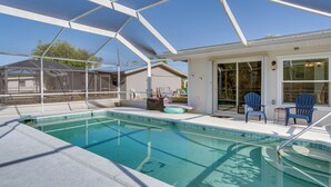 A swimming pool with a covered area, two chairs, and a small table.