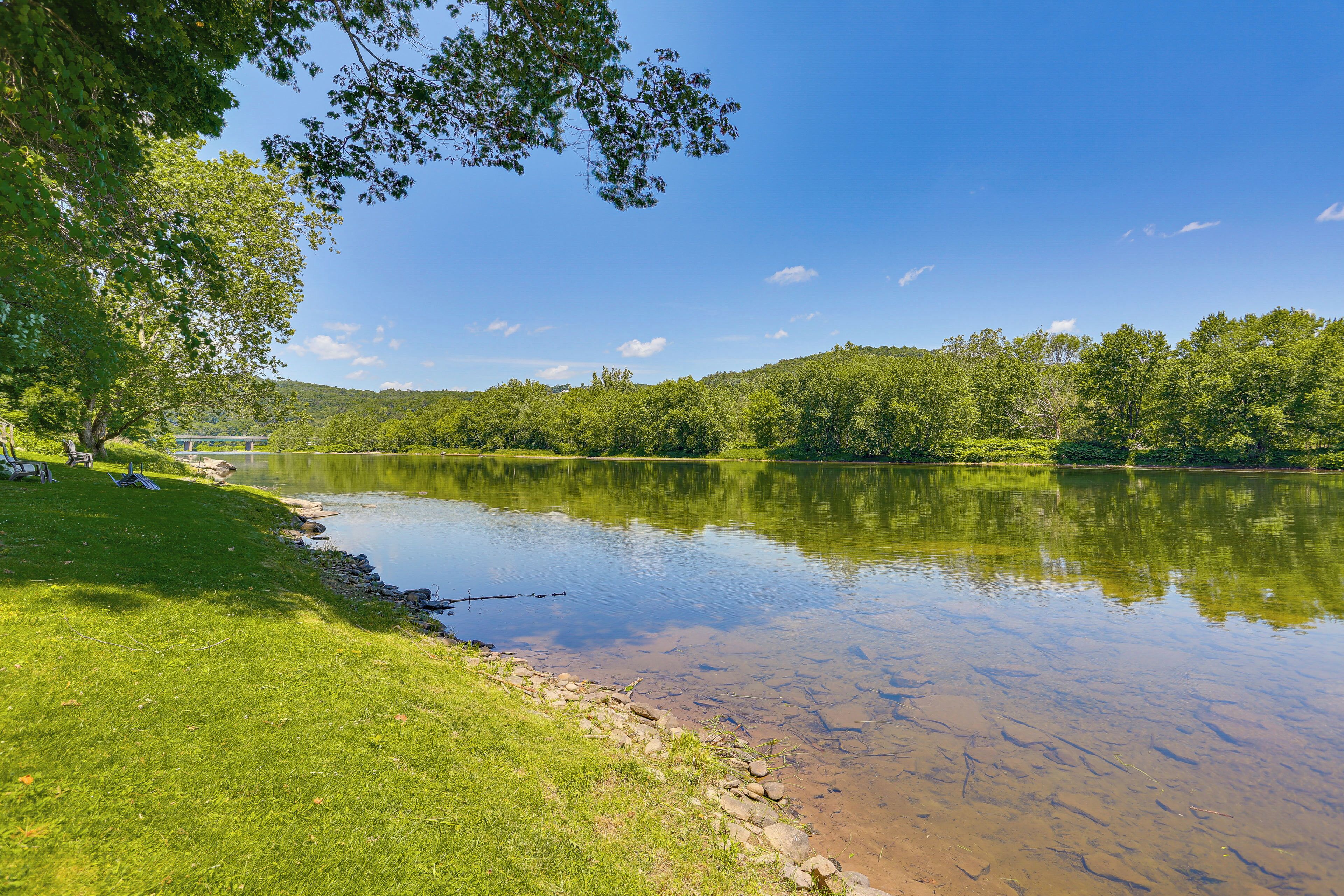 A calm lake with a grassy bank and trees, a clear sky, and a distant building.