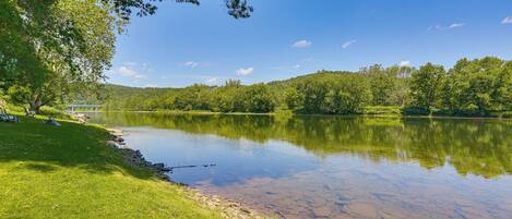 A calm lake with a grassy bank and trees, a clear sky, and a distant building.