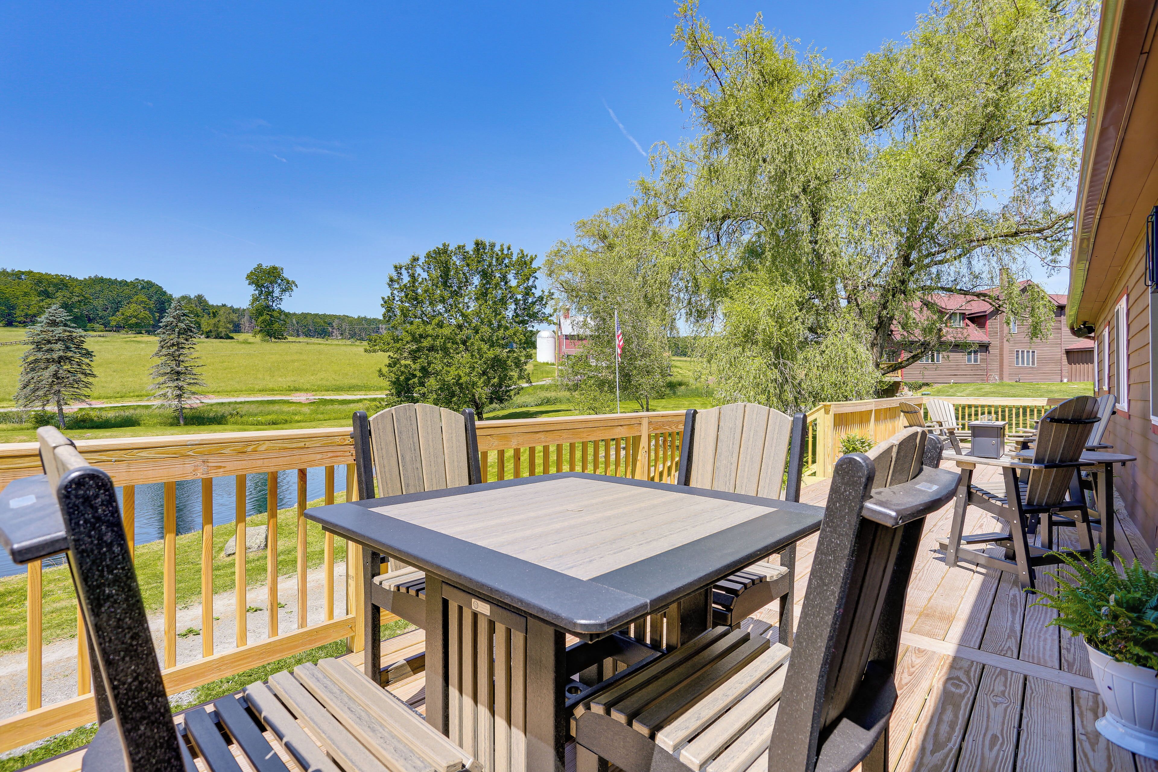 A wooden deck with a table and chairs, overlooking a grassy area and a body of water.
