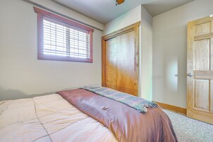 Un dormitorio con cama, ventana con persianas, puerta de madera y suelo alfombrado.