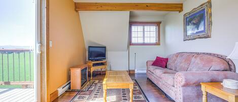 A living room with a wooden coffee table, a sofa, a television on a stand, and a window with blinds.