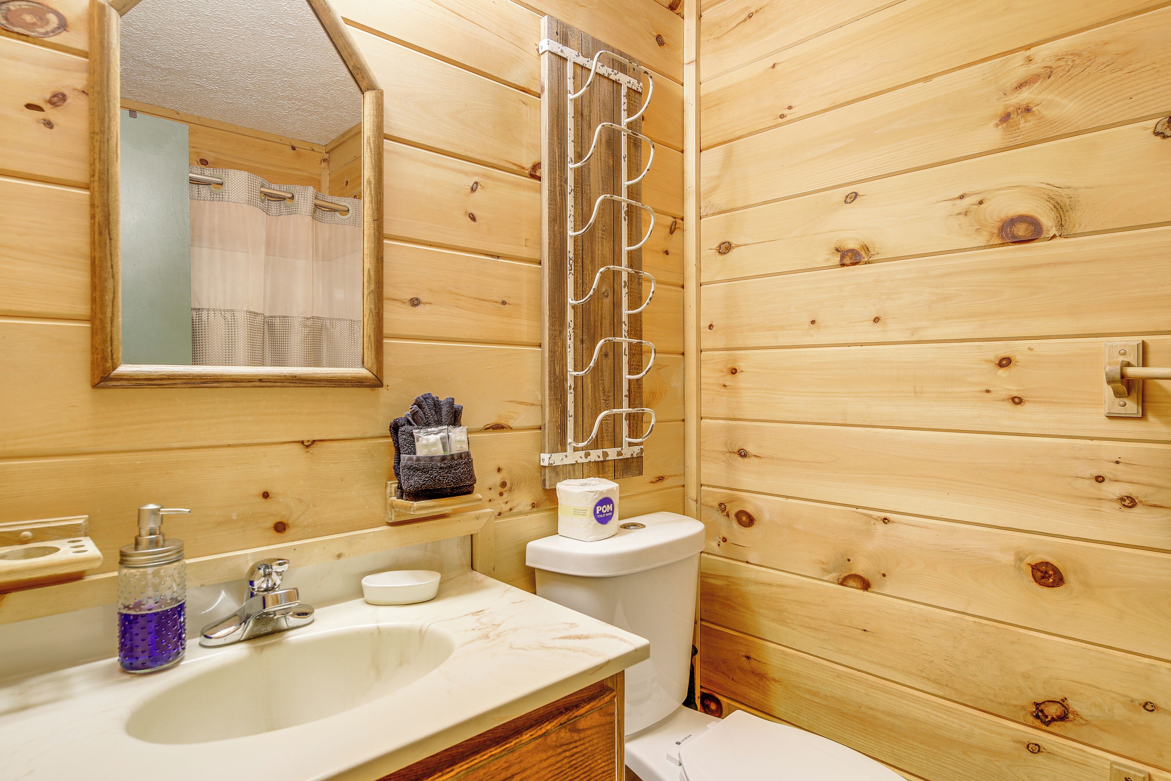 Une salle de bain rustique, aménagée dans une cabane en bois, avec un lavabo, un miroir, des toilettes et un rideau de douche.