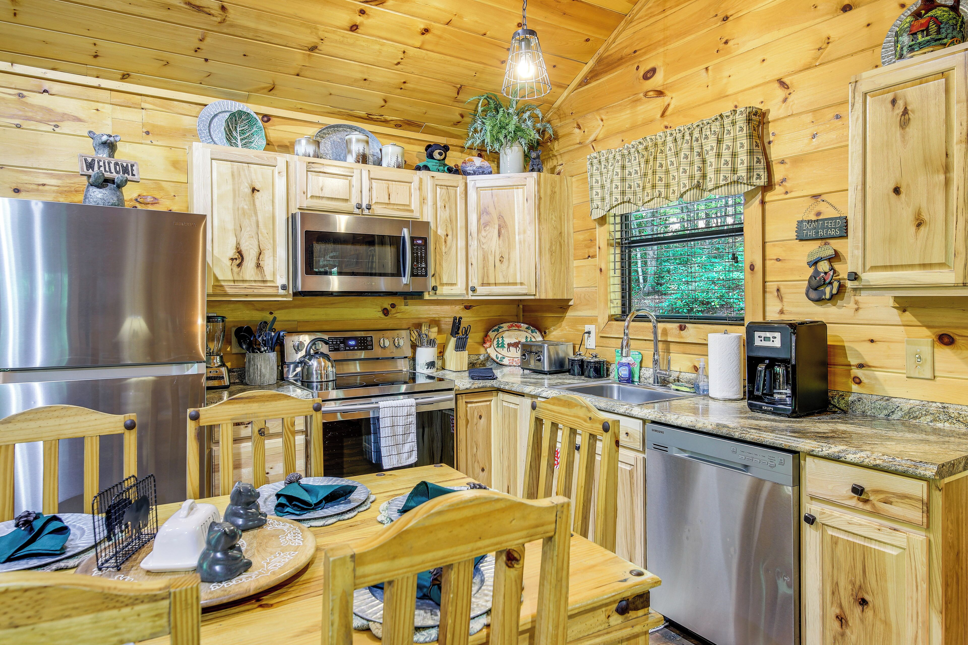 A wooden cabin kitchen with a stainless steel refrigerator, microwave, and dishwasher. There are wooden cabinets, a dining table with chairs, and various kitchen utensils and decorations.