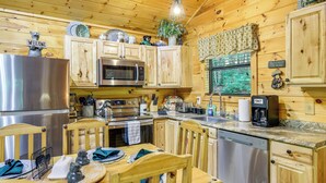 Eine Holzhütte mit einer Küche, die einen Edelstahl-Kühlschrank, eine Mikrowelle und einen Geschirrspüler beinhaltet. Es gibt Holzschränke, einen Esstisch mit Stühlen sowie verschiedene Küchenutensilien und Dekorationen.