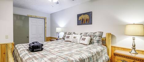 Une chambre à coucher comprenant un lit, une commode en bois, une table de chevet, un ventilateur de plafond, une porte et une lampe fixée au mur.