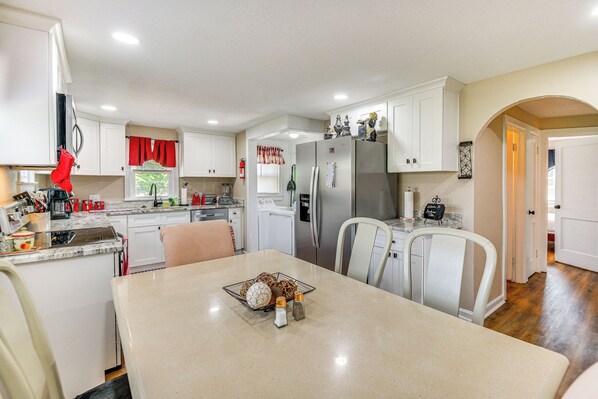 A modern kitchen with white cabinetry, a stainless steel refrigerator, and a dining area with a marble countertop.