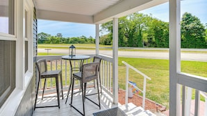 A covered porch with a table and chairs, a view of a road and greenery.