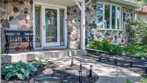 A stone house with a porch, a bench, and a garden with plants and a pathway. - 2 Mi to Dtwn Oshkosh: Canal Front w/ Dock! (Oshkosh)