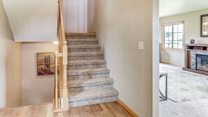 A carpeted staircase with a wooden handrail, a framed picture on the wall, and a fireplace in the adjacent room. - Black Hills Family Home: Close to Hiking Trails! (Blackhawk)