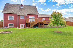 A two-story red house with a wooden deck and a tree in the yard.