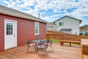 A wooden deck with a metal table and chairs, a bench, and a white door.