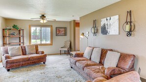 A living room with a brown leather sofa, a wooden coffee table, and a ceiling fan. There is a bookshelf with plants and a framed picture on the wall. - Black Hills Family Home: Close to Hiking Trails! (Blackhawk)